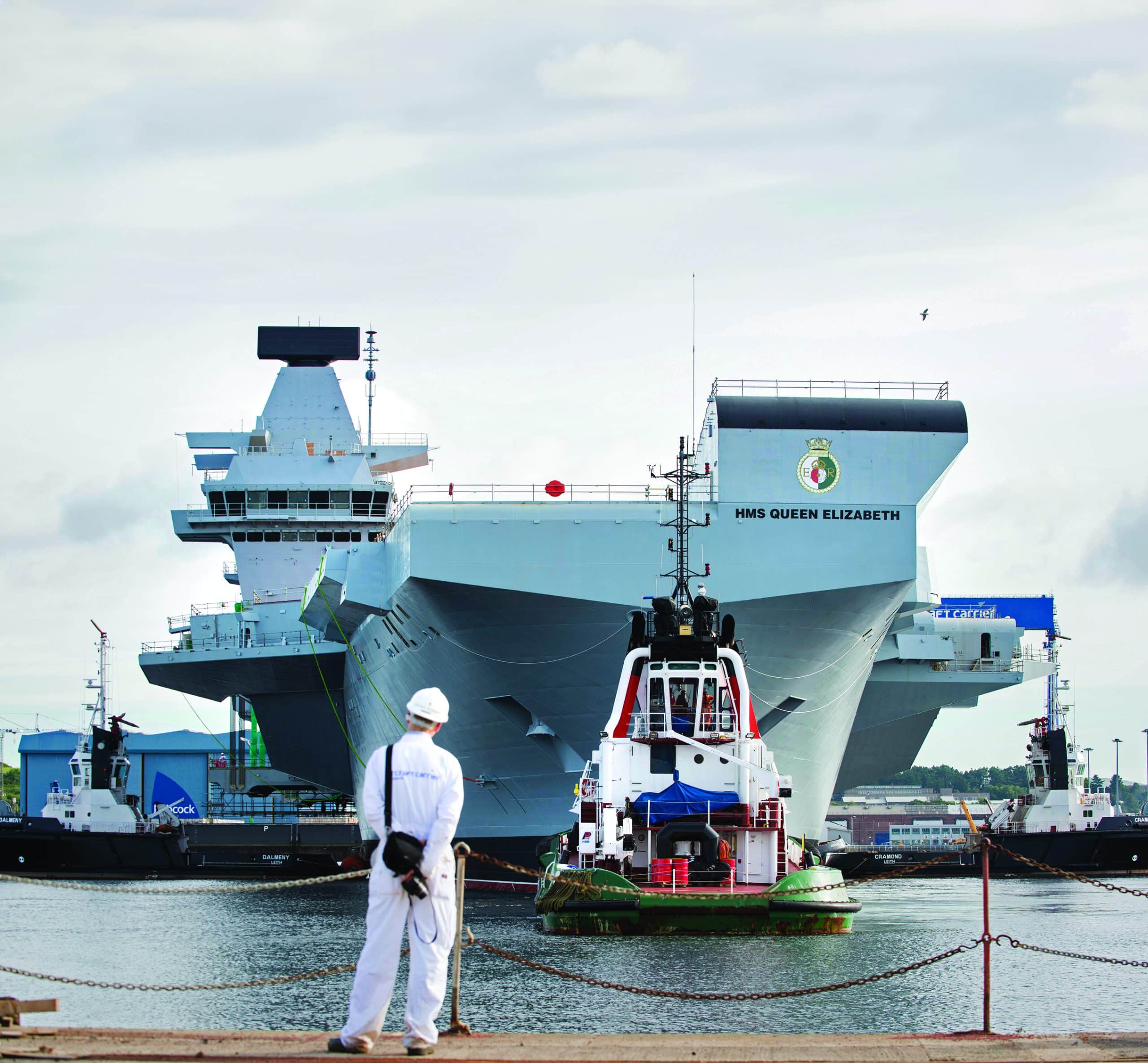 HMS QEC docked behind man standing with PPE