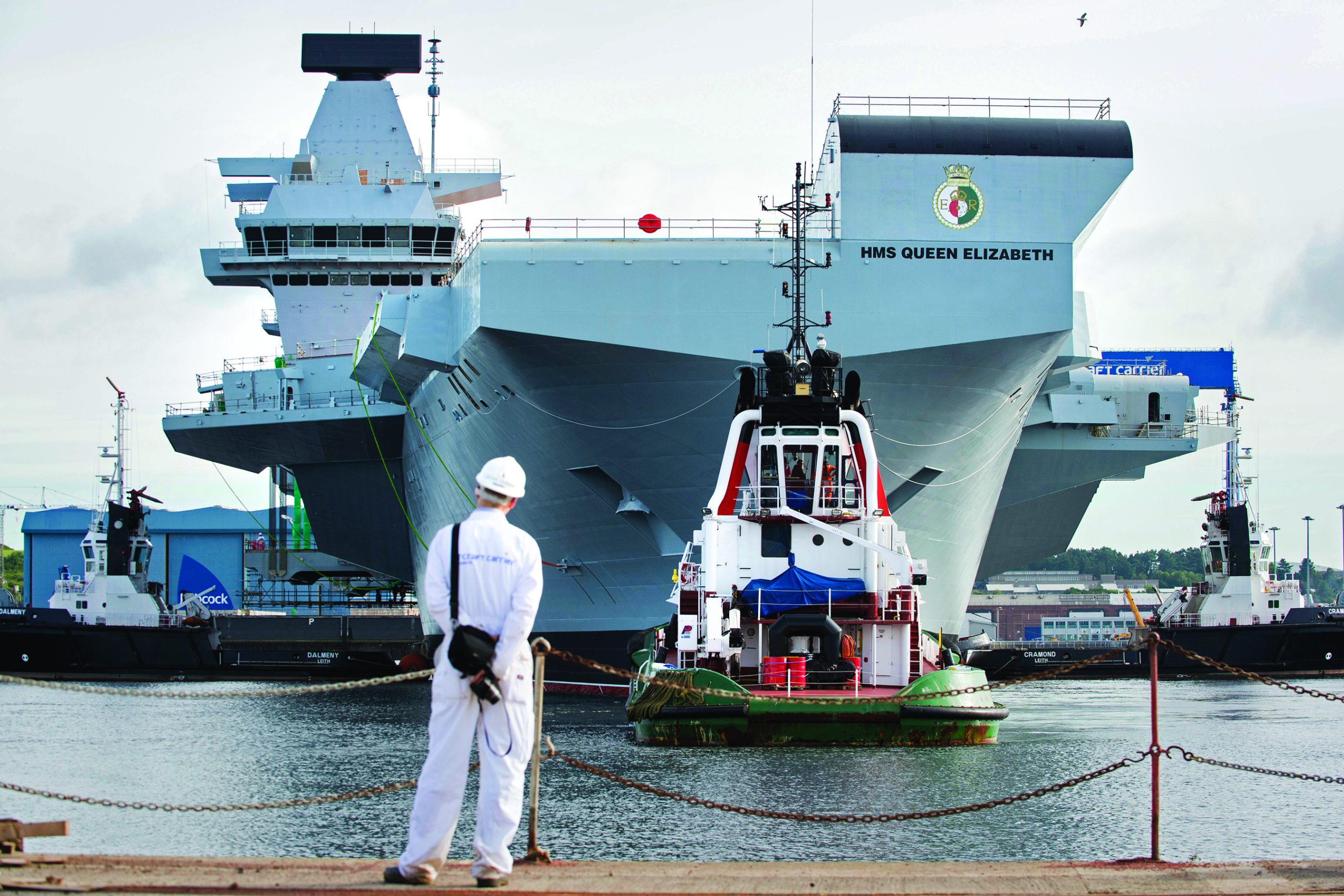HMS QEC docked behind man standing with PPE
