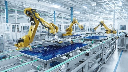 Yellow robotic arms working on solar panel in factory setting