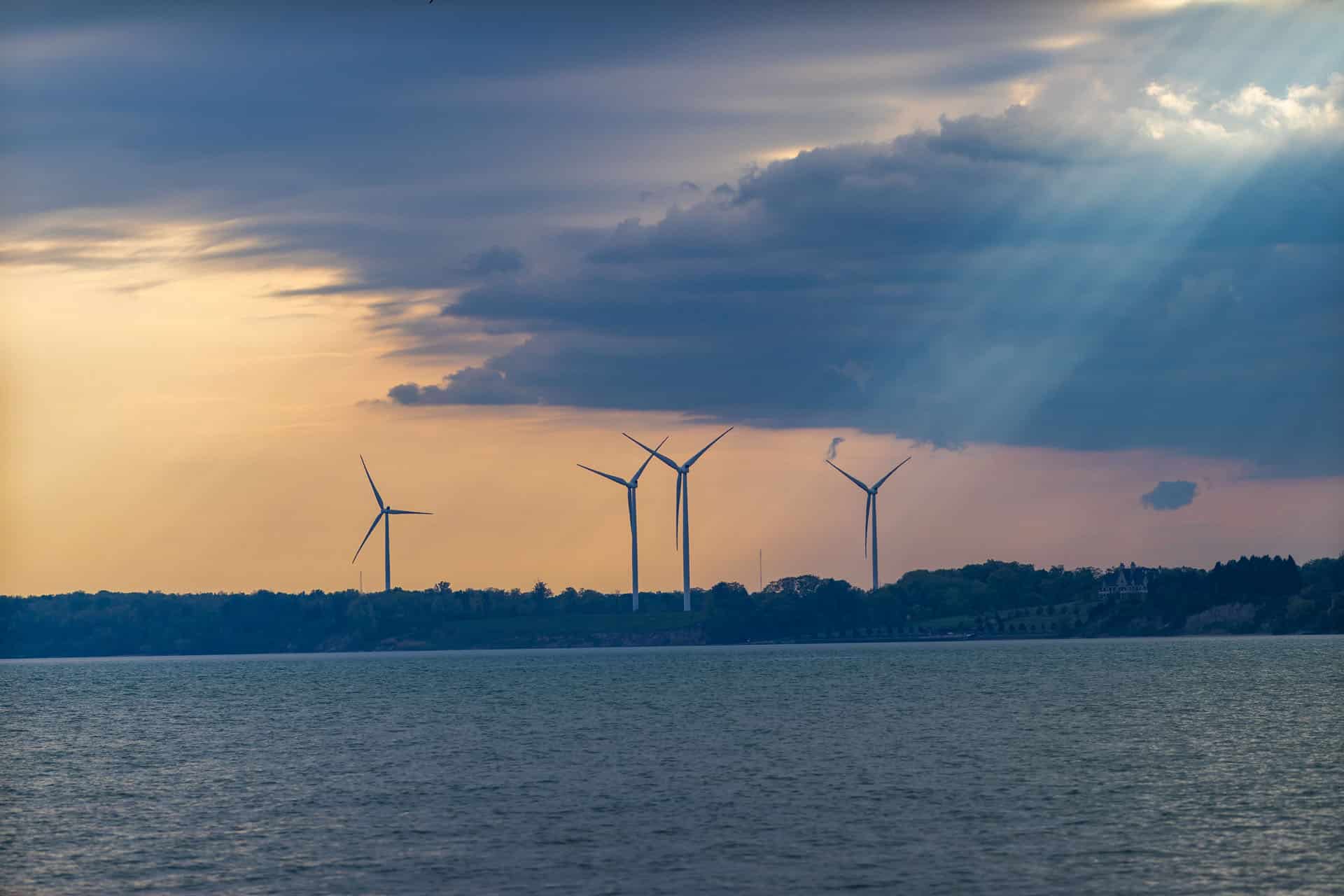 Wind turbines on shore with water in front of them sunset