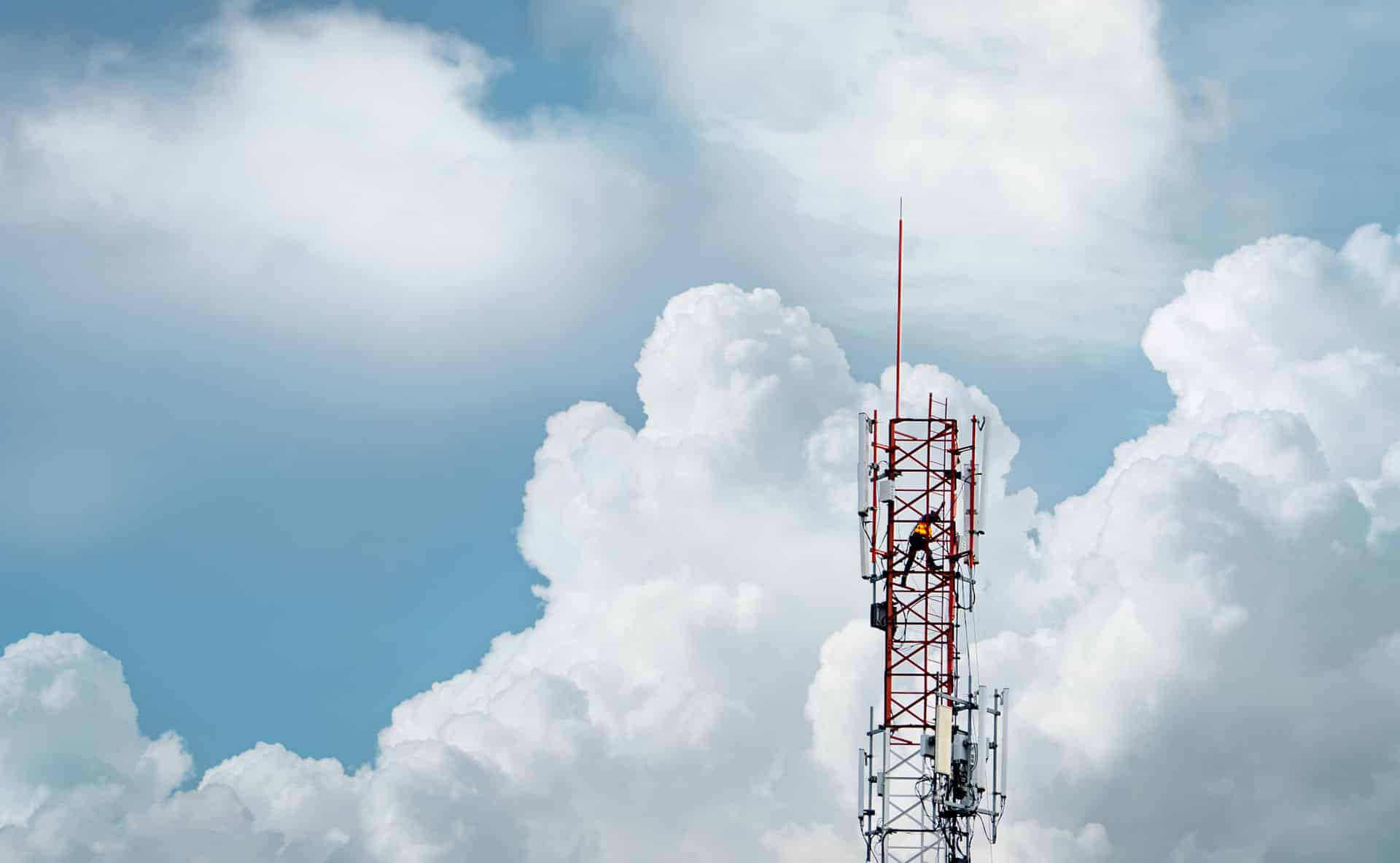 Top of telecommunication tower against a cloudy sky with person climbing up it